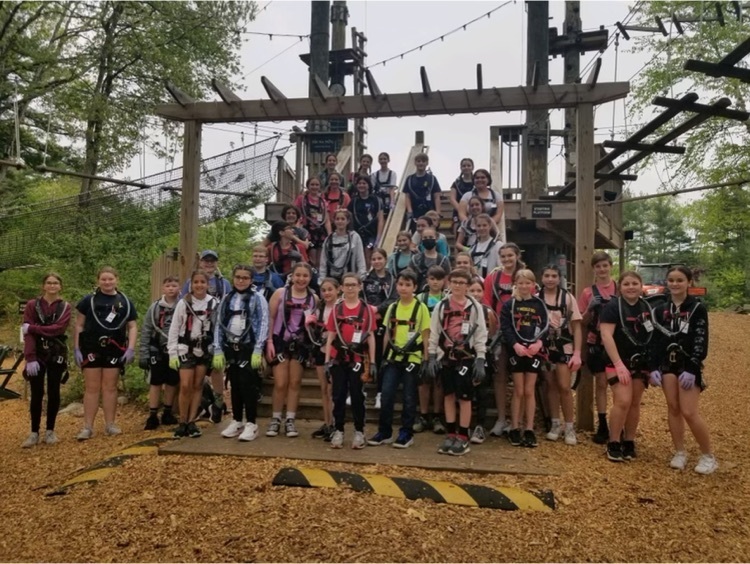 groups of students in harness gear standing in front of the rope course for a photo 