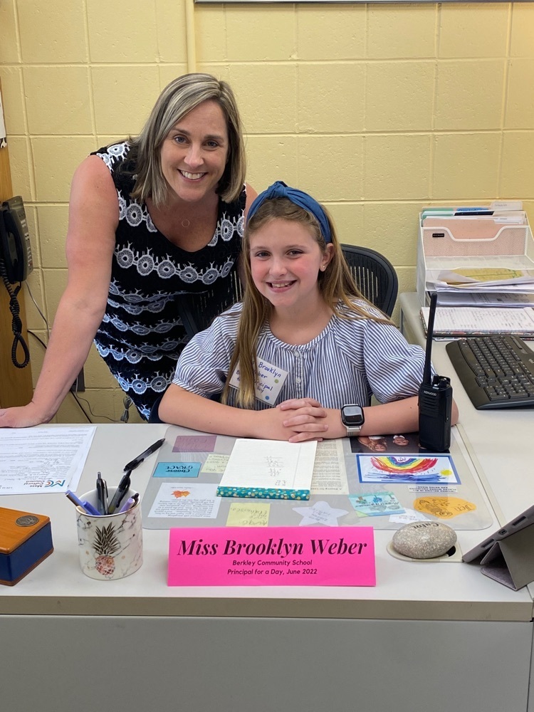 student sitting at the principal desk with the principal standing behind her