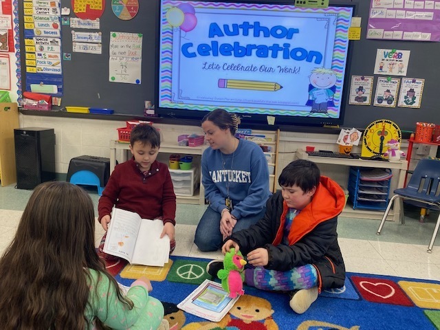 Teacher sitting on the floor with students sharing their books